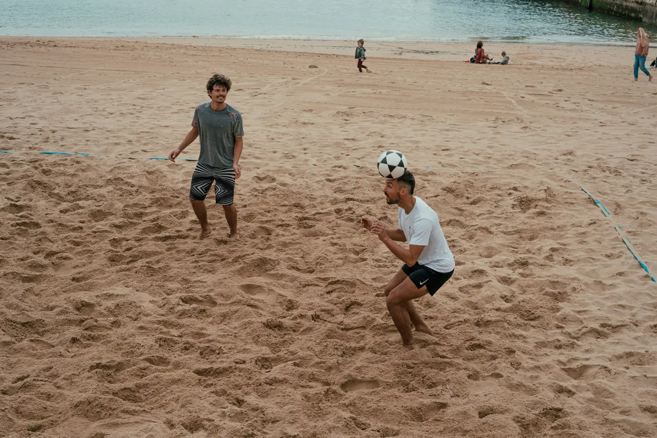 Dois jogadores de futevôlei na areia, um deles cabeceando a bola