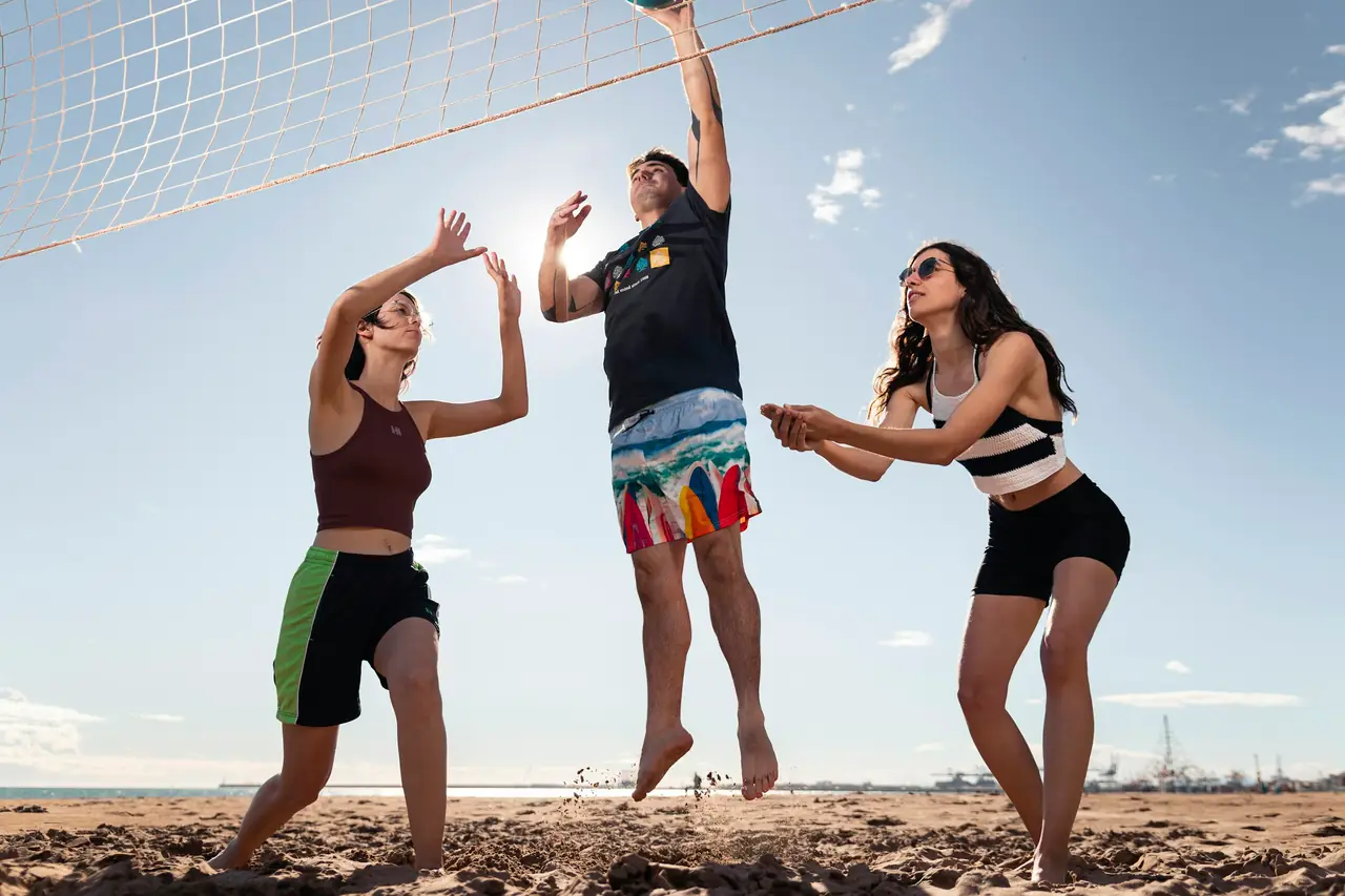 Three beach volleyball players going for the ball at the net